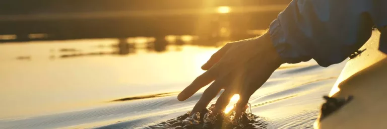 A hand touching water while travelling in a canoe.
